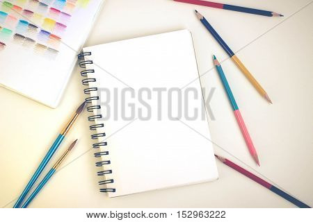 Top view of art supplies on white table. Colored pencils, paintbrushes and sketchbook.  May be used as product mockup.