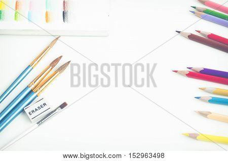 Top view of art supplies on white table. Colored pencils, paintbrushes and sketchbook.  May be used as product mockup.