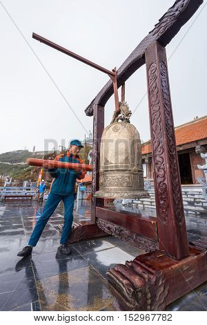 Sa Pa Vietnam - September 18 2016: Staff man in blue uniform ring a big golden bell in front of temple of Fansipan legend of Sa Pa Vietnam.