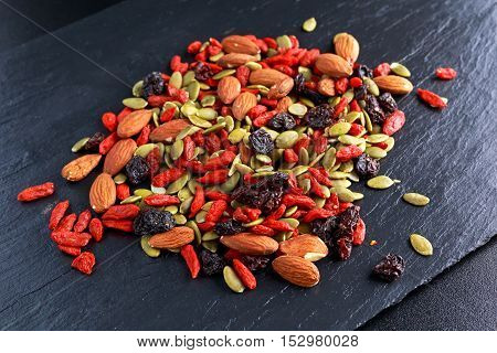 Nut mix snack with raisins, pumpkin seeds, almonds and goji berries on stone board.