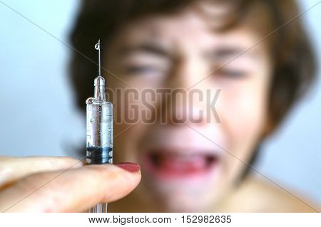 doctor holding a syringe with injection vaccination. Boy is afraid. Teen boy in fear of injection.