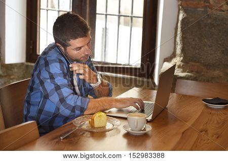 young attractive businessman or student on his 30s wearing casual clothes working or studying with laptop computer at coffee shop busy talking on mobile phone in modern business concept