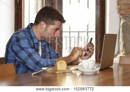 young attractive businessman or student on his 30s wearing casual clothes working or studying with laptop computer at coffee shop busy typing on mobile phone in modern business concept