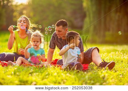 Happy Family In The Park- Young Family With Children Blow Soap Bubbles Outdoor