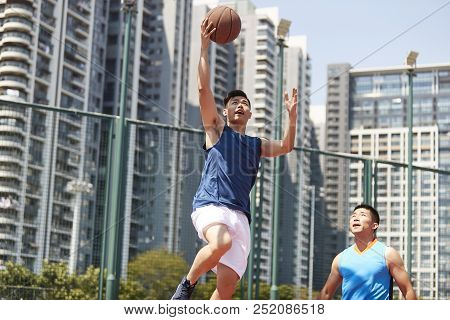 Young Asian Basketball Player Going Up For A Layup While Opponent Playing Defense.