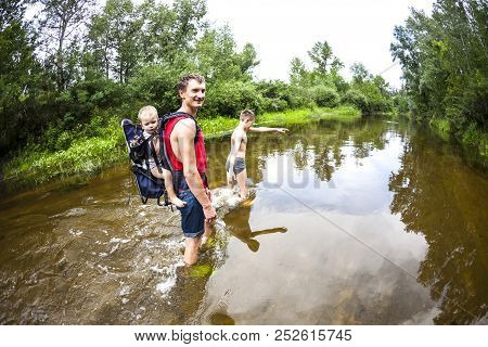 A Man With A Children Crosses The River. The Father Carries The Son In A Backpack. Rescue From Flood
