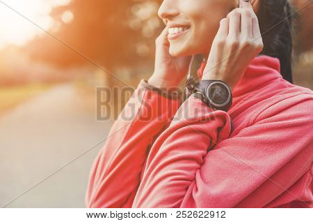 Female Athlete Insert Headphones. During Running. Woman Closeup. Fitness In Autumn Park. Wellness Co