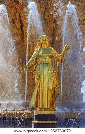 Moscow, Russia - August 01, 2018: Gilded Bronze Girl Against Golden Sheaf Of Wheat With Technical He