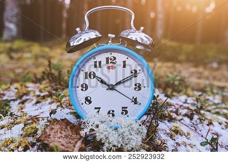 Vintage Blue Alarm Clock On Winter Forest Background. Daylight Saving Time Concept Winter Time, Tone