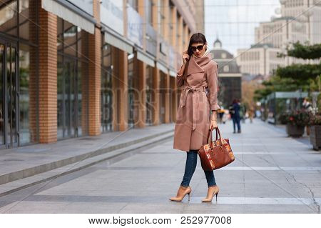 Beautiful Brunette Young Woman In Nice Brown Beige Coat, Jeans And Sunglasses. High Heels Shoes. Spi