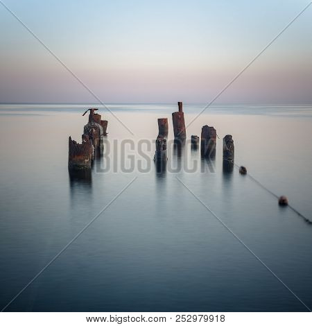 Long Exposure. Piles Stick Out Of The Sea In The Evening Twilight. Square Frame.
