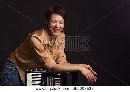 A Brunette In A Gold Shirt, With Short Haircut, On A Dark Kground Of The Studio. With Accordion Musi