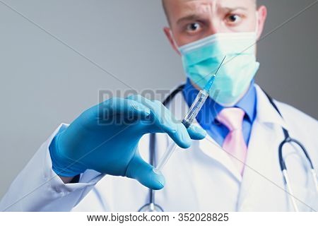 Scared Young Doctor In Gauze Mask And Medical Robe Holding Syringe In His Blue Rubber Glove Dressed 