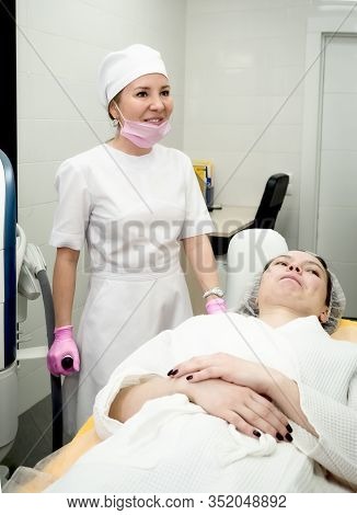 Woman Wearing Disposable Medical Bathrobe Being At Consultation In Cosmetology Clinic. Attractive Fe