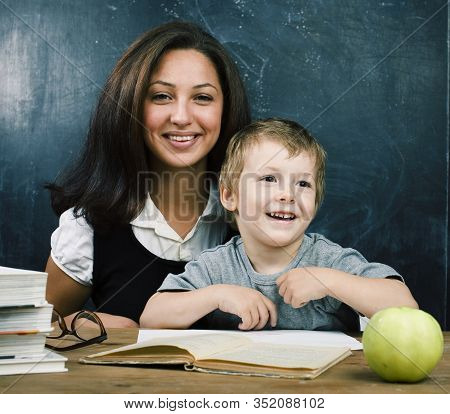 Little Cute Boy In Glasses With Young Real Teacher, Classroom Studying At Blackboard School Kido