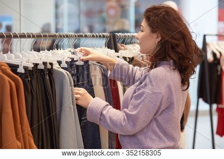 Shopping, Fashion, Style And People Concept. Young Darkhaired Woman Choosing Clothes And Looking For