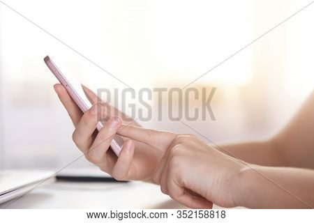 Side View Of Female Holding White Modern Smart Phone While Sitting At Table, Feceless Portrait Of Fe