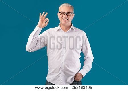 Im Fine. Smiling Senior Man In Specs Showing Ok Gesture Isolated Over Blue Studio Wall, Free Space