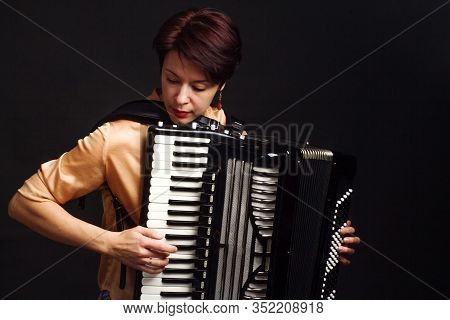 A Brunette In A Gold Shirt, With Short Haircut, On A Dark Kground Of The Studio. Play The Accordion
