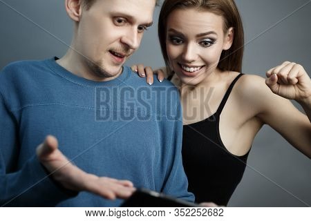 Man With The Girl Excitedly Looking At The Smartphone. Are In An Agitated State. Emotions Of Experie