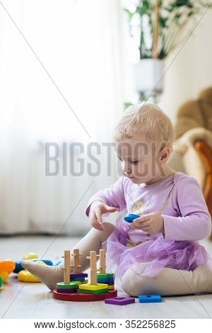 Girl Plays Toys In Living Room. Montessori Wooden Toy Folded Pyramid. Circle, Quadra, Triangle, Rect