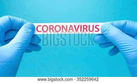 Coronavirus Background. Hands In Medical Gloves Hold A Piece Of Paper With Coronavirus Printed On It