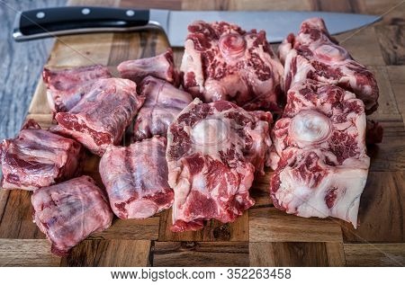 Several Raw Chopped Ox Tails On A Cutting Board With A Chefs Knife