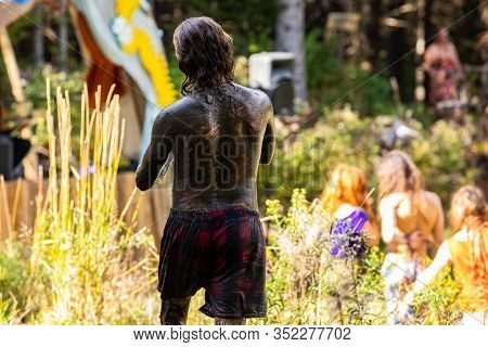 A Shirtless Man Is Seen From Behind, Body Covered In Mud After Bathing In Lake During A Festival Cel