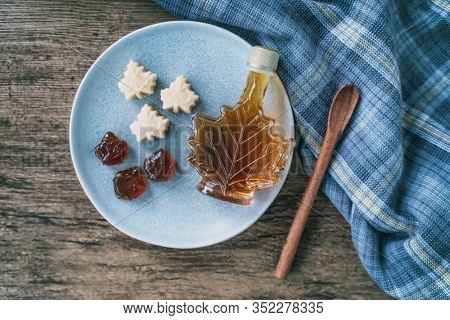 Maple syrup top view of organic natural product from Canada. Maple leaf shape bottle, soft candy and hard candy taffy on rustic wooden kitchen table and spoon for cooking