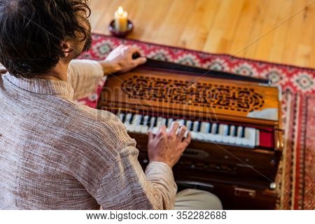 Rear View Of Young Shamanic Male Musician Playing Harmonium For Sacred And Kirtan Music With Burning