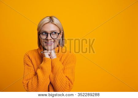 Charming Caucasian Blonde Girl Is Looking Aside Through Her Eyeglasses Holding Her Hand Near The Chi