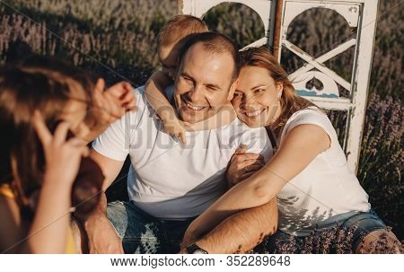 Charming Caucasian Family Sitting In A Lavender Field Posing Happily While Embracing Each Other