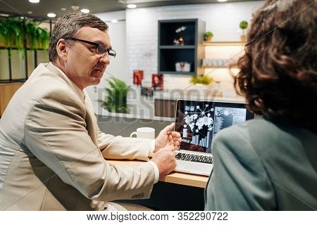 Serious Mature Entrepreneur In Glasses Showing Digram With Sales Data To Colleague