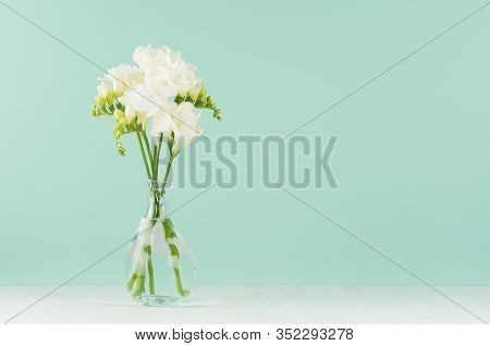 Fresh White Freesia Flowers In Elegant Transparent Vase On Soft Light Green Mint Menthe Wall And Whi