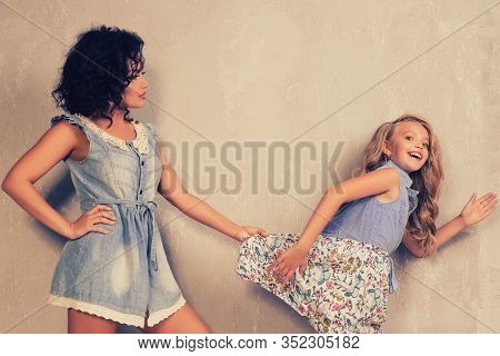 An Adult Mother Holds A Running Daughter For A Dress Near Grey Wall