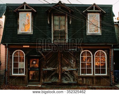 An Old Brown And Black Wooden Home With Trees And Sunlight Reflecting Off The Windows