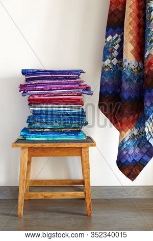 Stack Of Fabriсs On A Stool And Quilt Top Made In The Bargello Style On Neutral Wall Background