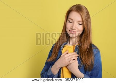 Beautiful Grateful Woman With Hands On Chest Against Yellow Background. Space For Text