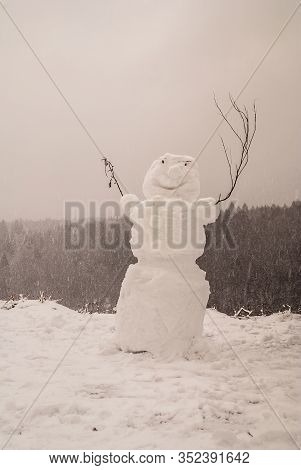 Snowman With Hands Made Of Branches During A Snowfall On A Forest Background.