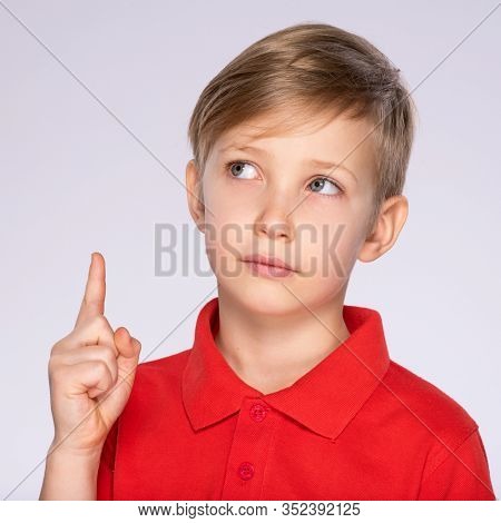 Portrait of thinking boy with good idea -  isolated over white background. 8 year old kid pointing finger up. Thoughtful child points by finger upward. Pensive boy in a red t-shirt thinking about