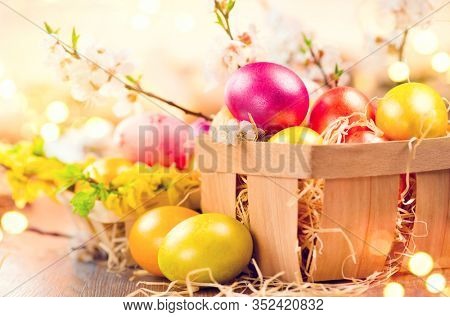 Easter colorful eggs in the basket. Beautiful colourful yellow, pink and orange color eggs with decorations and spring blossoming flowers over bright blurred bokeh, spring holidays background