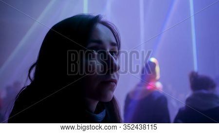 Close Up View: Portrait Of Woman Looking At Bright Light Laser Show In Dark Room Of Museum Or Exhibi