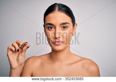Young beautiful brunette woman holding dental aligner orthodontic to teeth corretion with a confident expression on smart face thinking serious