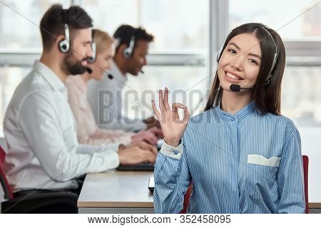 Asian Female Operator Shows Ok Gesture. Smiling Cheerful Japaneese Girl Working In Call Center Opera