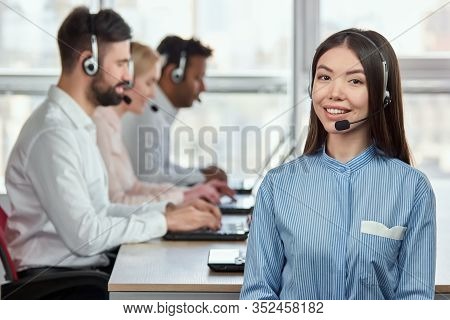 Portrait Of Smiling Japaneese Girl With Headset In Call Center Office. Asian Woman In Striped Shirt 