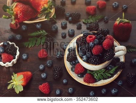 Tea Cup With Berries On A Dark Wooden Background. Raspberry, Blackberry, Bilberry In A Cup. Beautifu