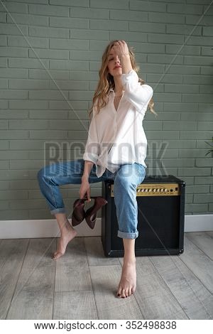 Young Beautiful Woman Sitting On Subwoofer With Bare Feet Next To Green Plant
