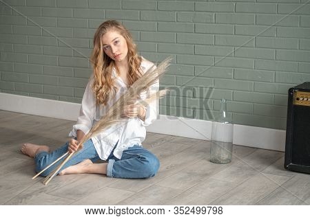 Young Beautiful Woman With Bare Feet Sitting On The Floor Next To Subwoofer And Glass Vase With Dry 