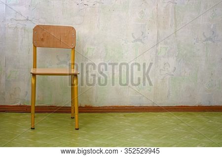 Lonely Children's Wooden Chair Near The Wall With Faded Soiled Shabby Wallpaper In A Child Care Faci