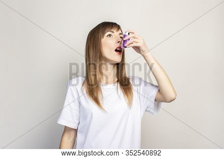 Young Woman Holds An Inhaler In Her Hand And Sprays On A Light Background. Banner. Concept For Easie